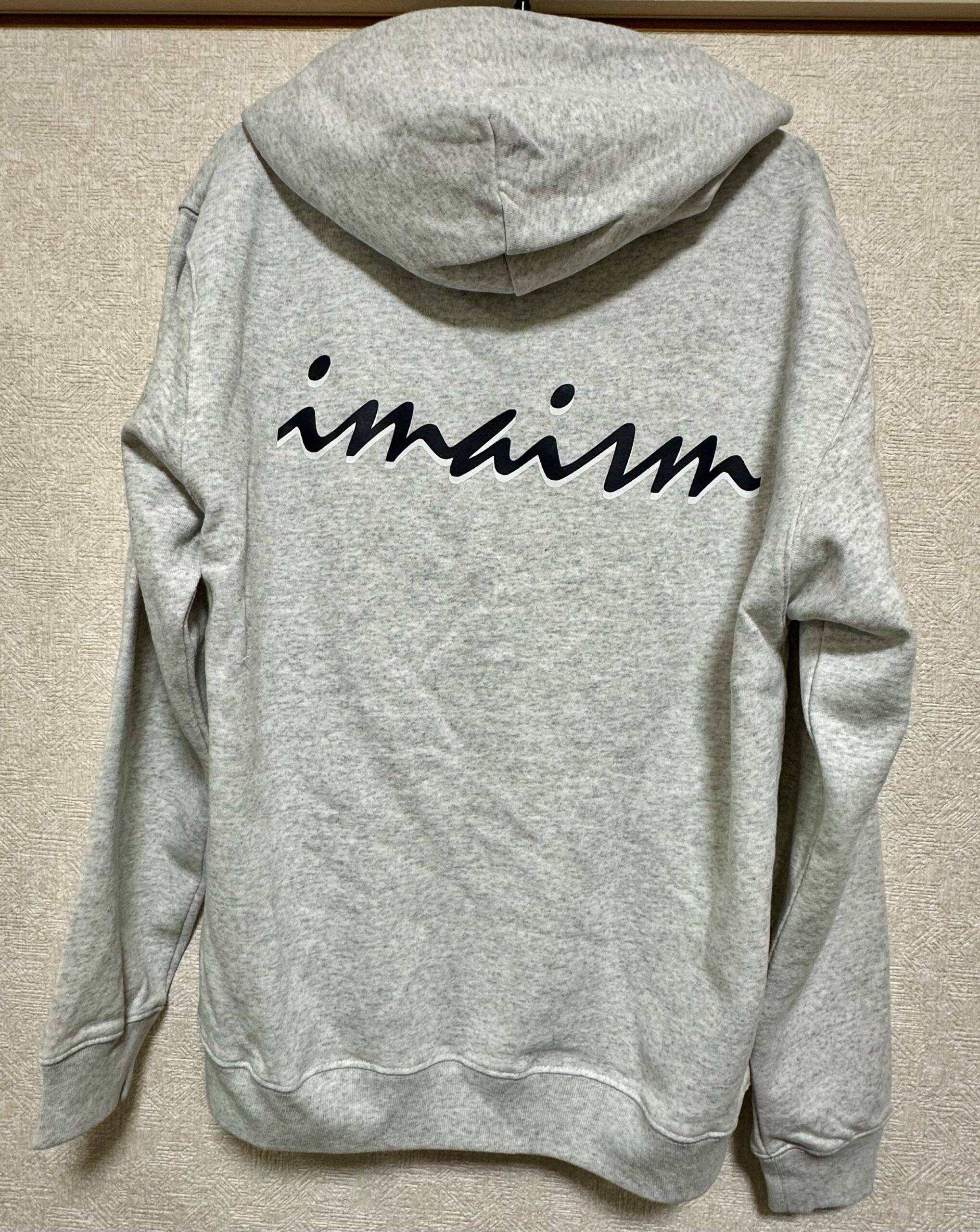 グレーのパーカー背面に黒いimaismロゴを配した実物