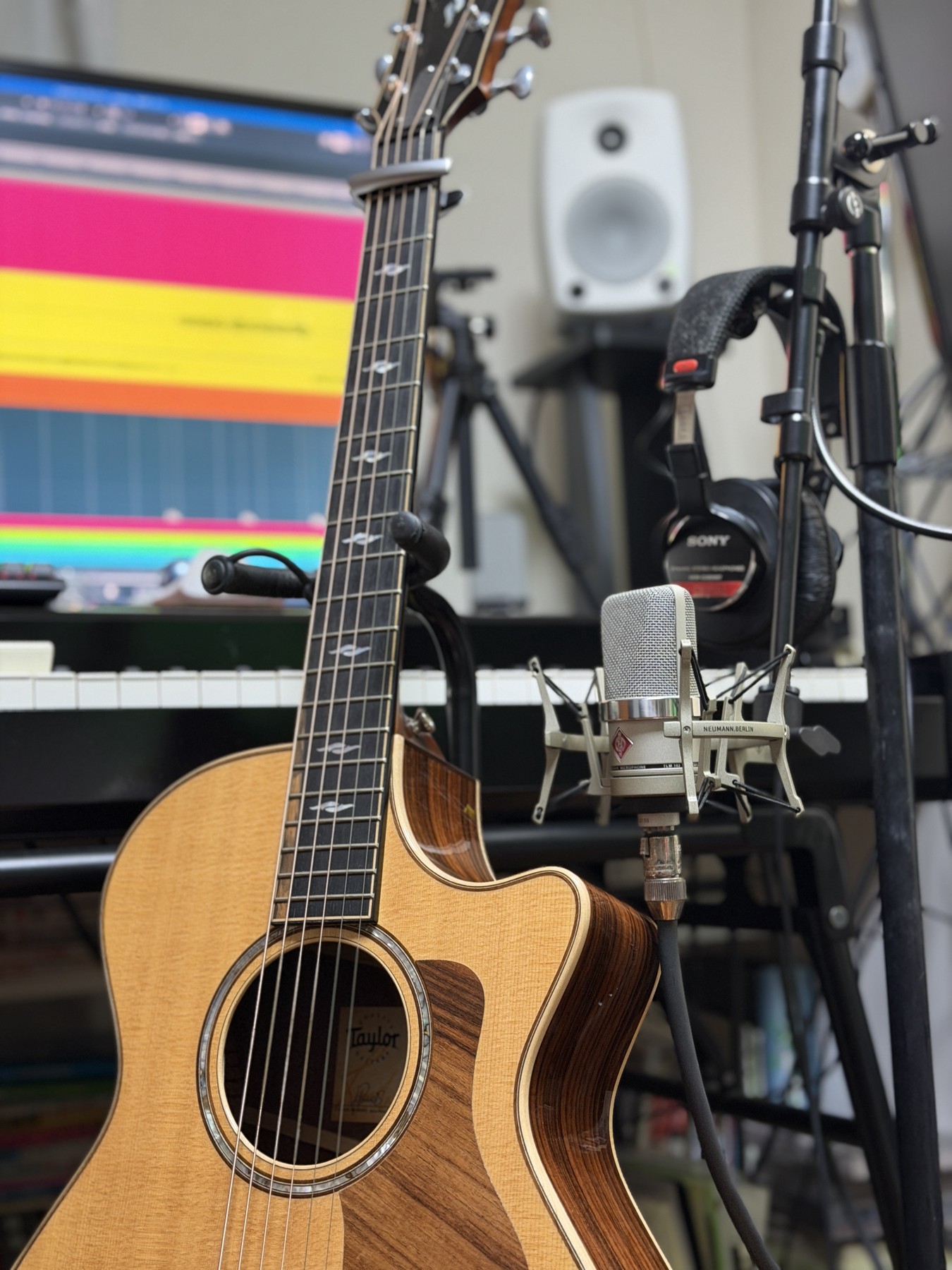 NowMusicの制作風景。アコースティックギターとマイク、奥に制作画面とモニタースピーカー