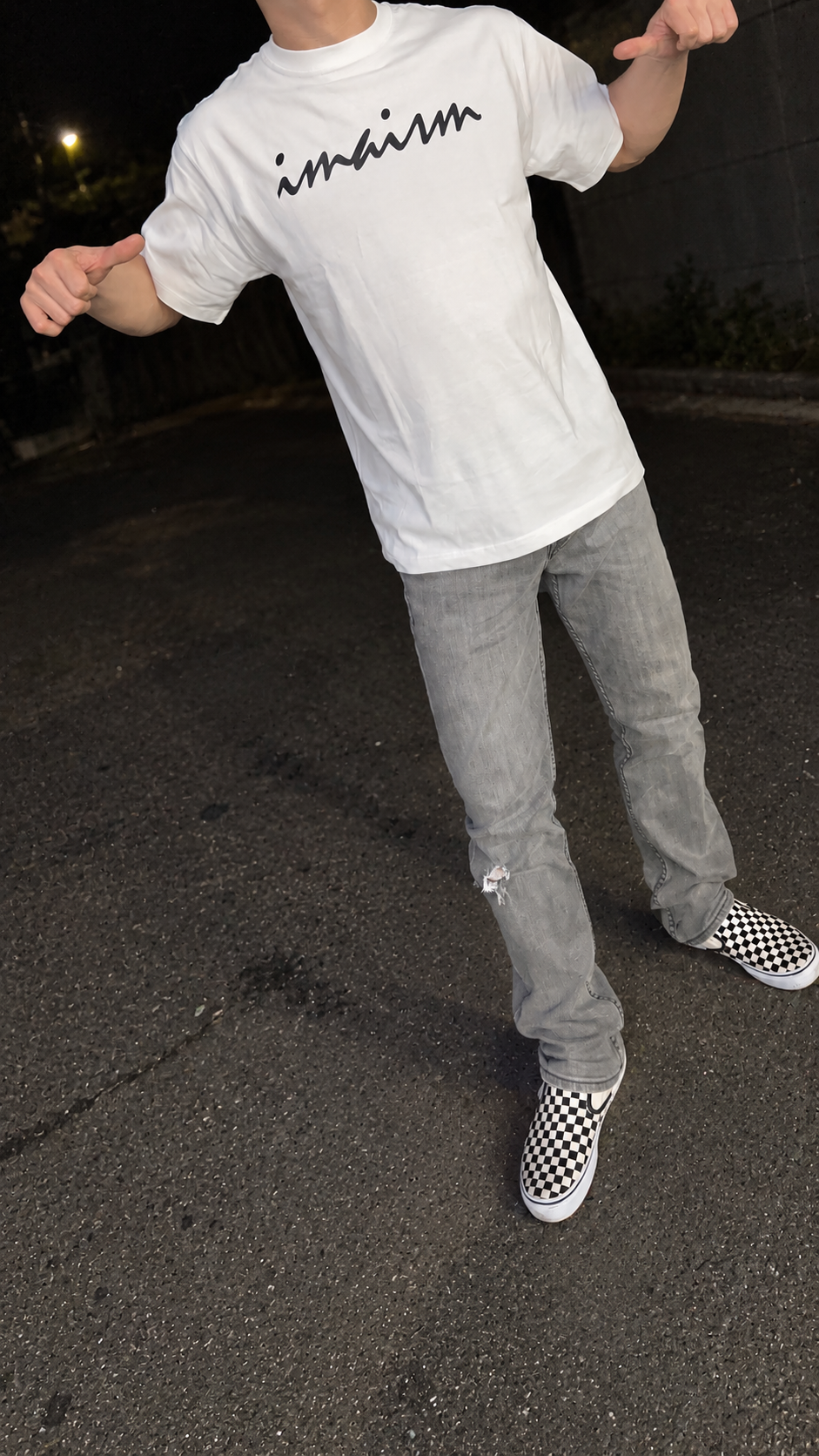 imaismの白いロゴTシャツを着たストリートスナップ風の着用イメージ。顔は写らない構図
